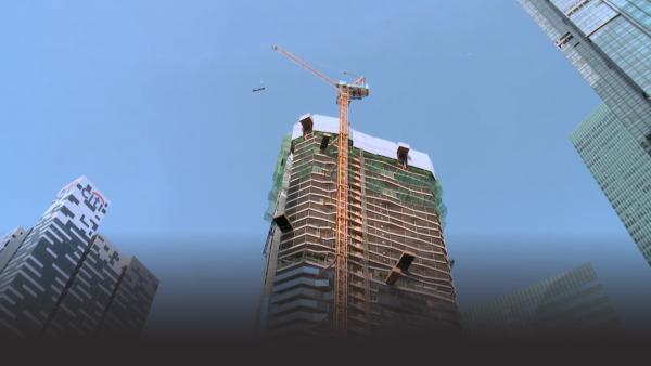 A tower crane lifts a load to the top of highrise construction project