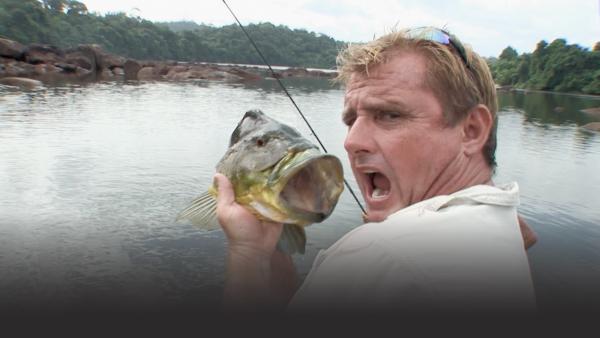Man holds up a large bass next to his head, imitating the large mouth of the bass