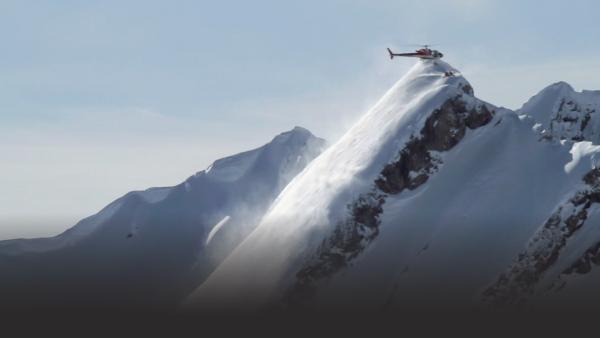 Helicopter drops off several skiers on a mountain peak