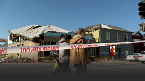 Young couple walks by a building leveled by an earthquake