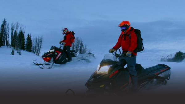 Two men ride snowmobiles