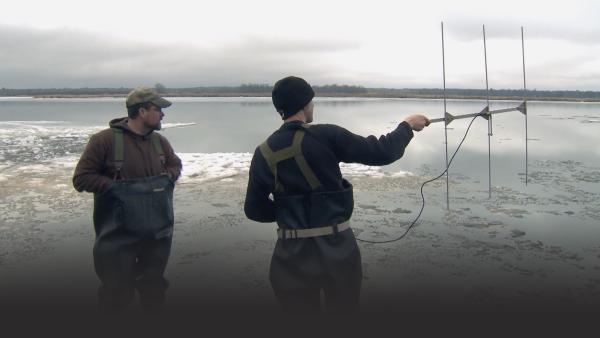Two men stand in icy water.