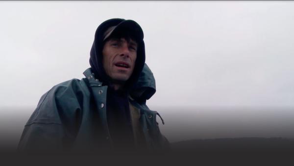 A fisherman looks into the camera in cloudy weather.
