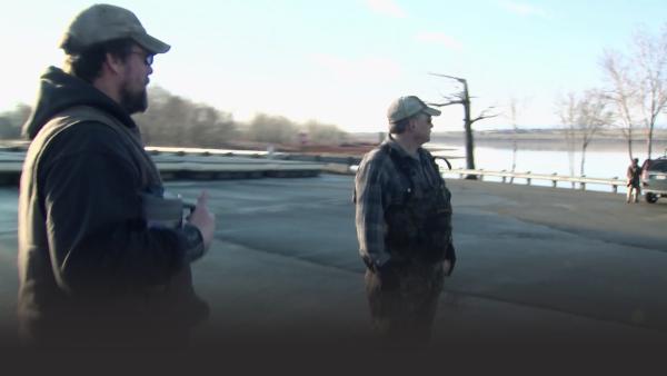 Two fishermen look at the water.