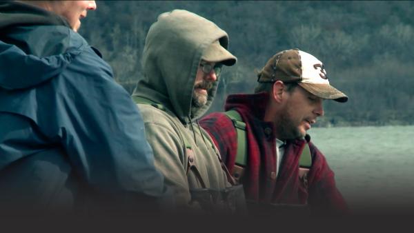Three fishermen look into the water.