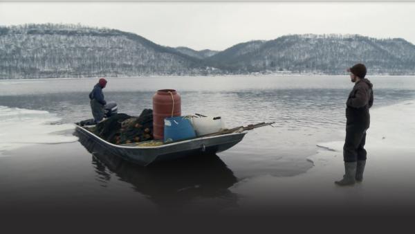 Two men move a boat into icy water.