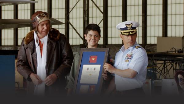Two men awarding a young man a plaque