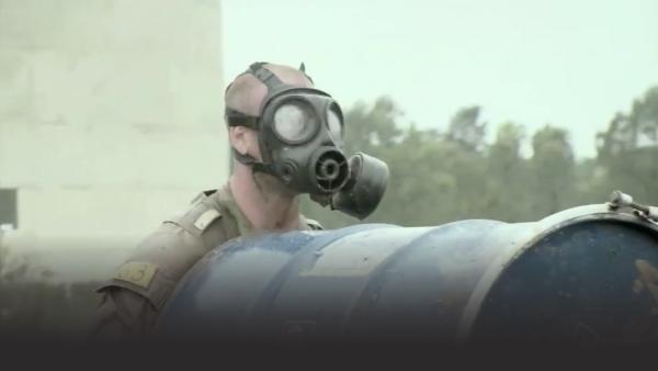 Man with gas mask carrying barrel