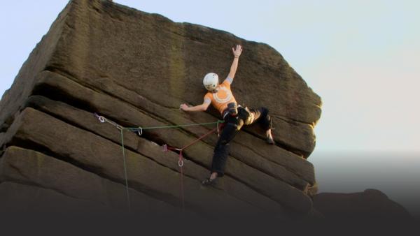 Woman reaches high for the top of a large rock