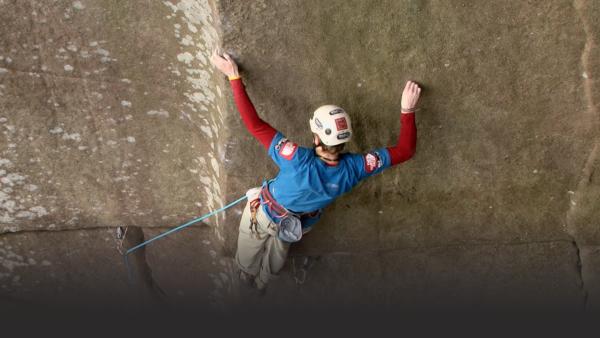 Man holds on to a vertical ledge to climb a cliff