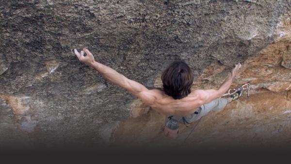 Man clings to rock face, muscles extended