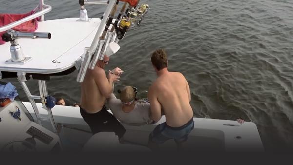 Two men pulling another man on their boat to save him 