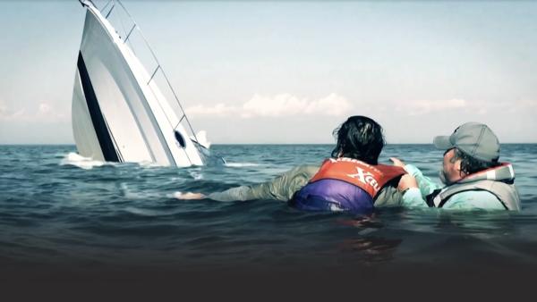 Two people stranded in the ocean watching their boat sink 