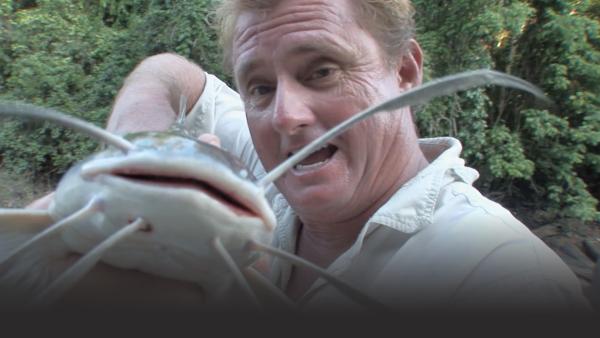 Man holds a catfish up into the camera to show off the whiskers