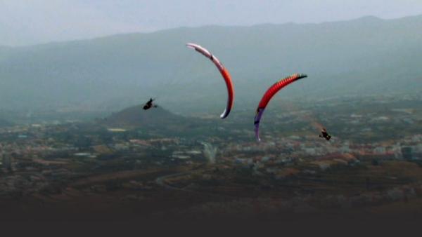 Two paragliders spiraling toward each other over city