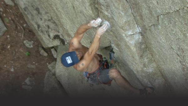 Man climbs a granite slab, both hands pulling himself up