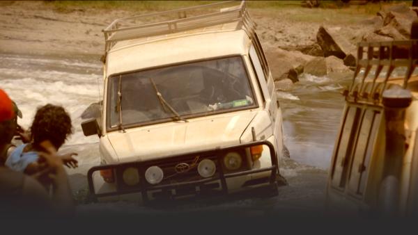 An SUV half submerged in a flooded river