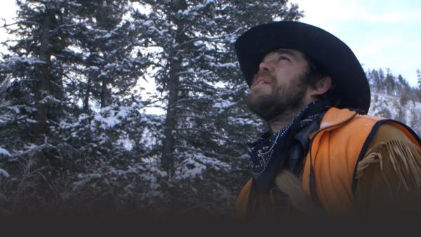 A man looks up in a snowy forest.