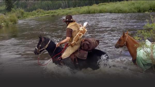 A man crosses a river on a horse.