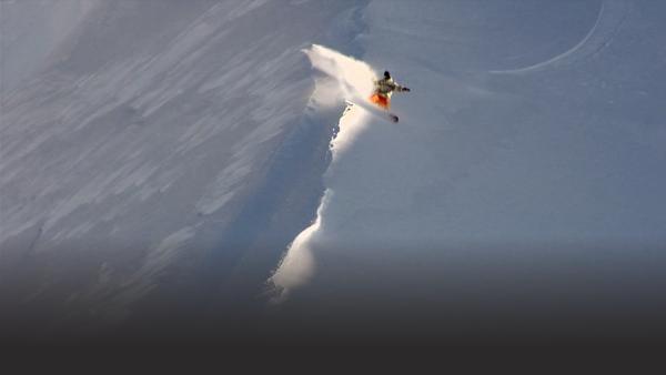 snowboarder turns at the edge of a cornice spraying snow behind him