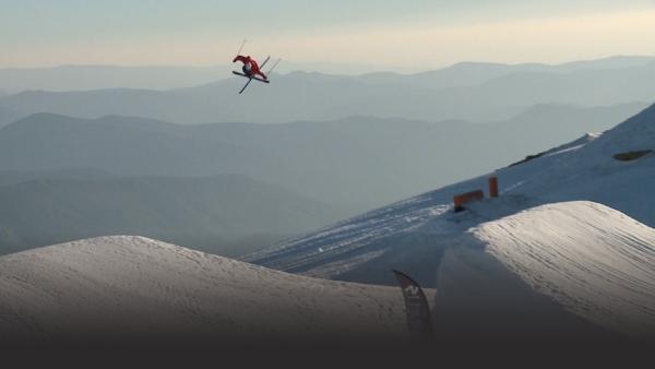 Skier high above a jump, mid twist, mountains in background