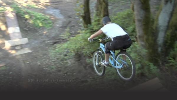 woman on a blue mountain bike leaps off a wooden bridge